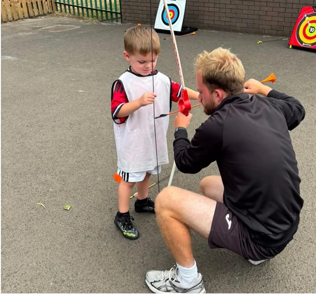 UK Sports coach supporting a child during an archery activity at a HAF camp