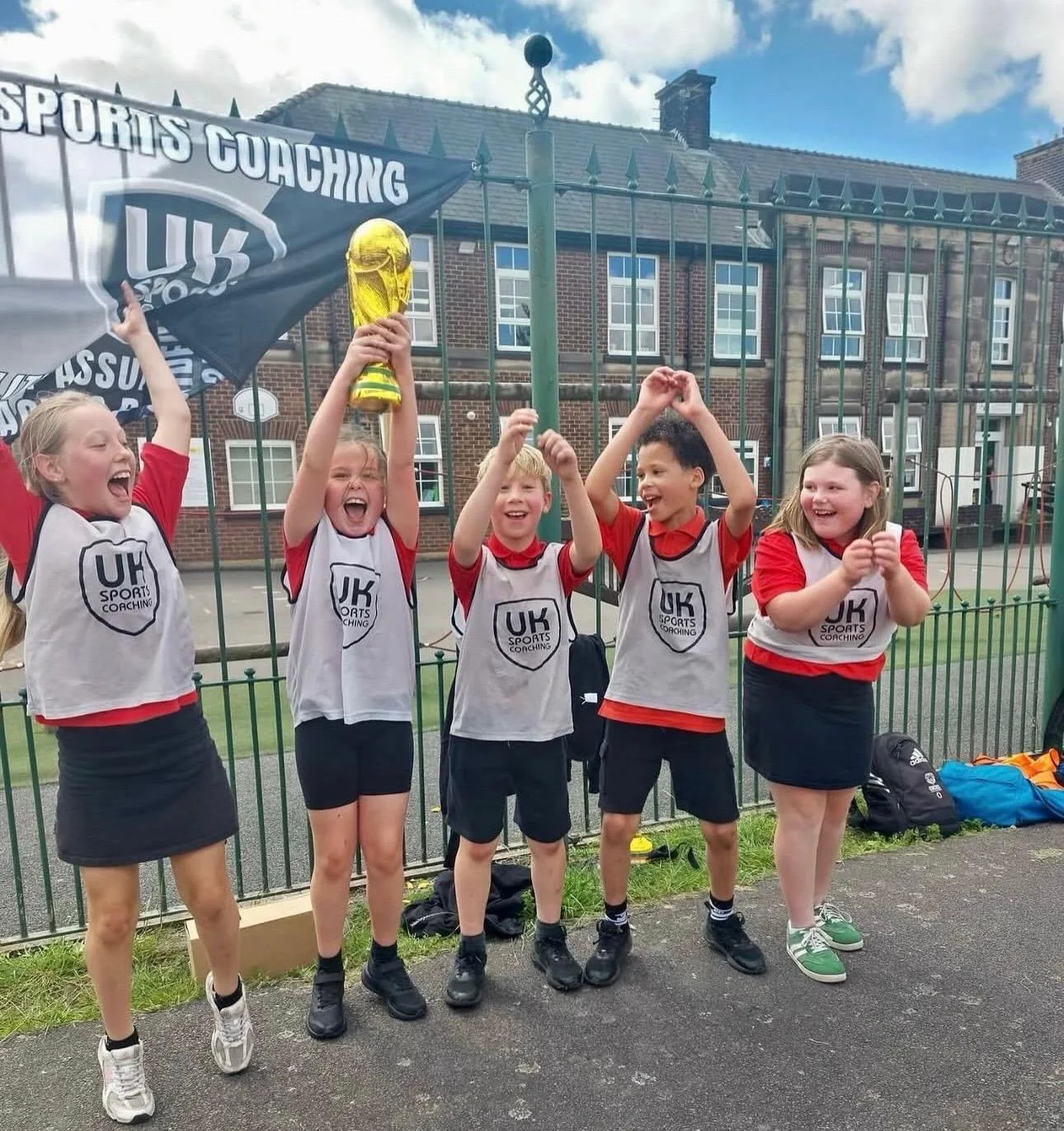 Primary school pupils celebrating together with a trophy during a UK Sports Coaching Ltd activity